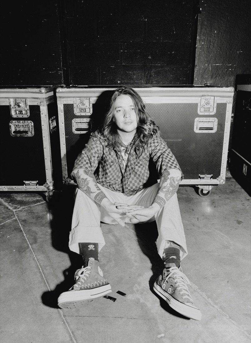 Billy Strings sitting backstage against a row of road cases