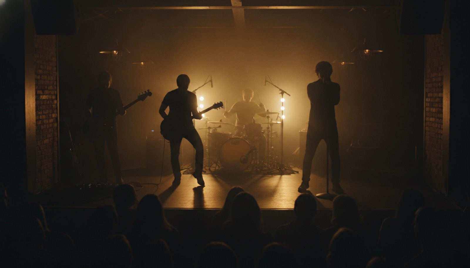 Four musicians in silhouette on a small, dimly lit club stage, warm stage lights behind them