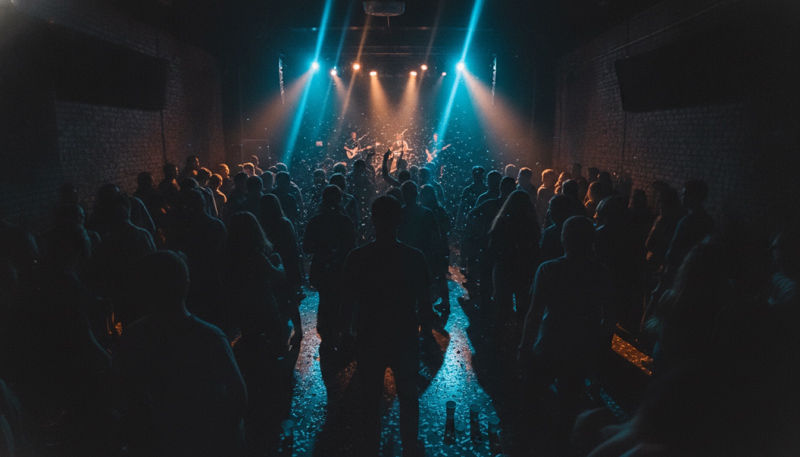 A small, packed club venue at night lit in cool blue and amber stage light, crowd silhouettes in the foreground