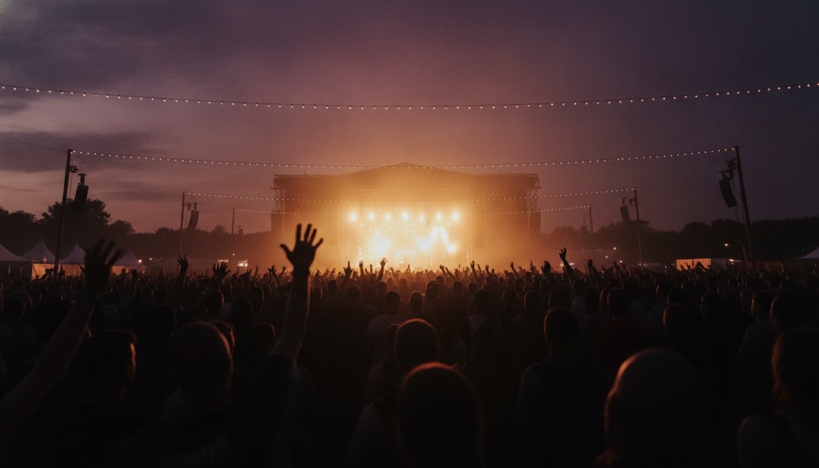 Vast silhouetted festival crowd at dusk facing a glowing stage