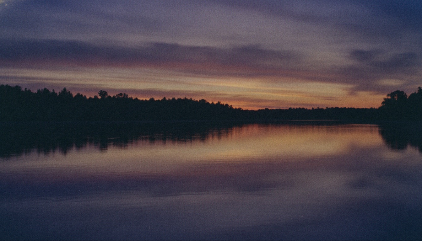 A wide calm river at dusk reflecting a purple and gold sky with a distant tree line