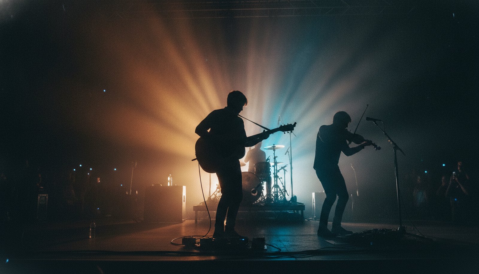 A three-piece acoustic band in silhouette on a dim stage, a guitarist, a violinist, and a drummer