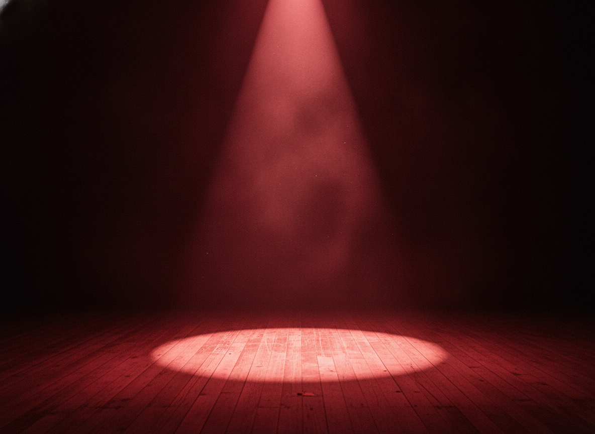 A lone spotlight cutting through darkness onto a bare wooden floor, deep red haze around the edges