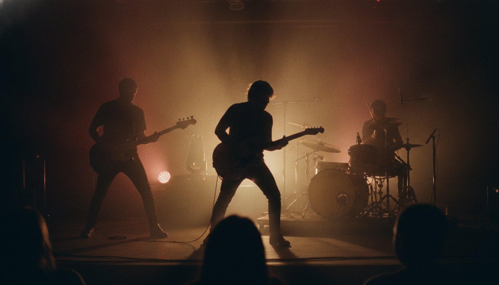 A three-piece blues-rock band in silhouette on a dim stage lit amber and red