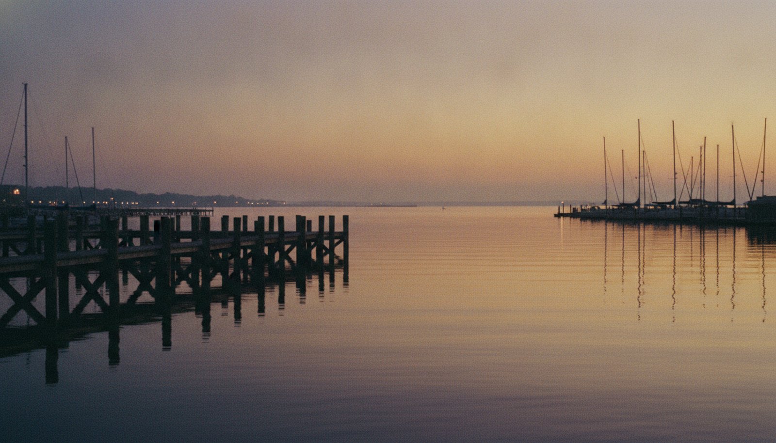 A Chesapeake Bay harbor at dusk, wooden docks and sailboat masts against an amber and violet sky
