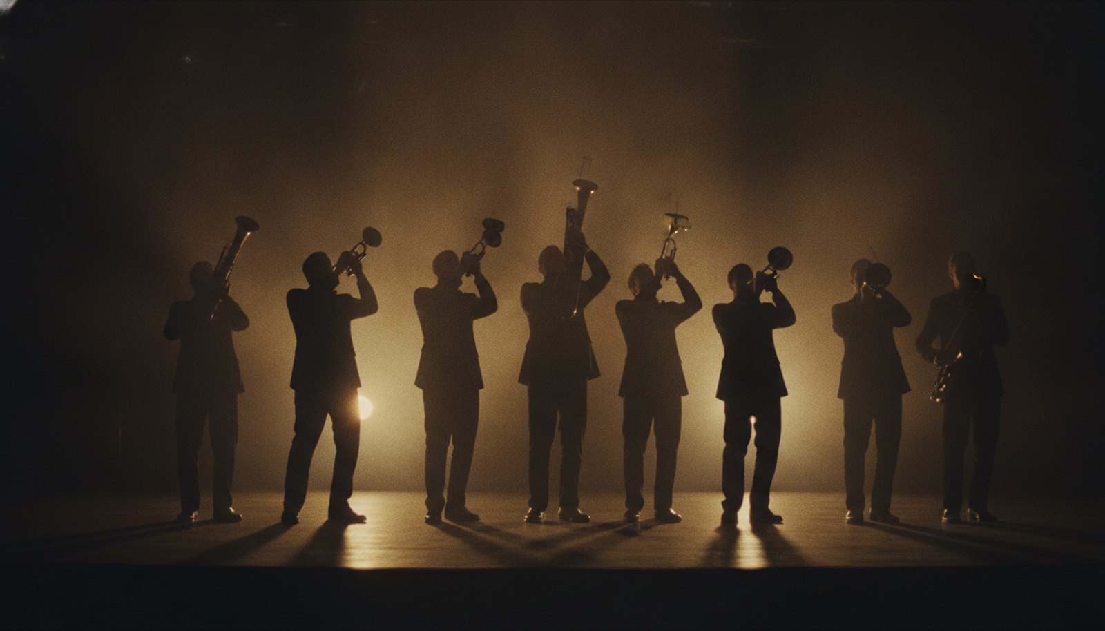 A big band horn section in silhouette on a dim stage, backlit by warm amber spotlights, no faces visible