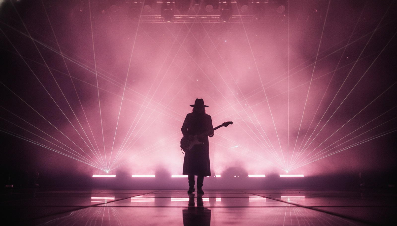 A lone silhouetted musician on a vast stage bathed in swirling pink and violet light and laser haze