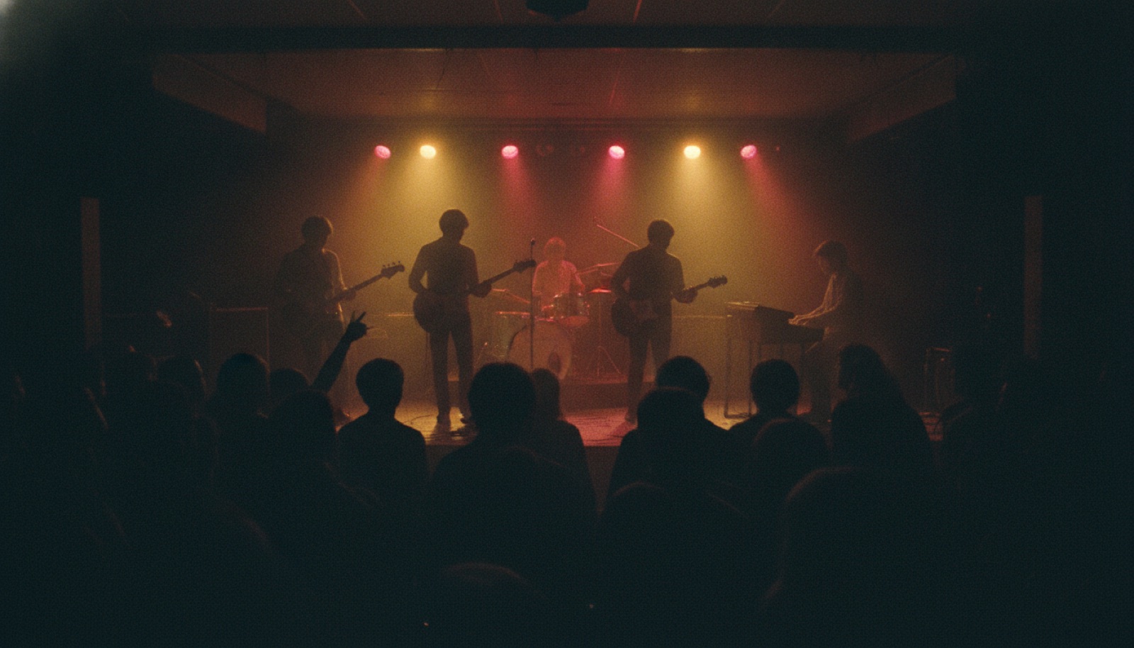 Four musicians in silhouette on a small club stage bathed in warm amber and red light