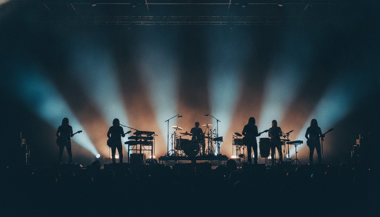 A six-piece band in silhouette against banks of stage lights