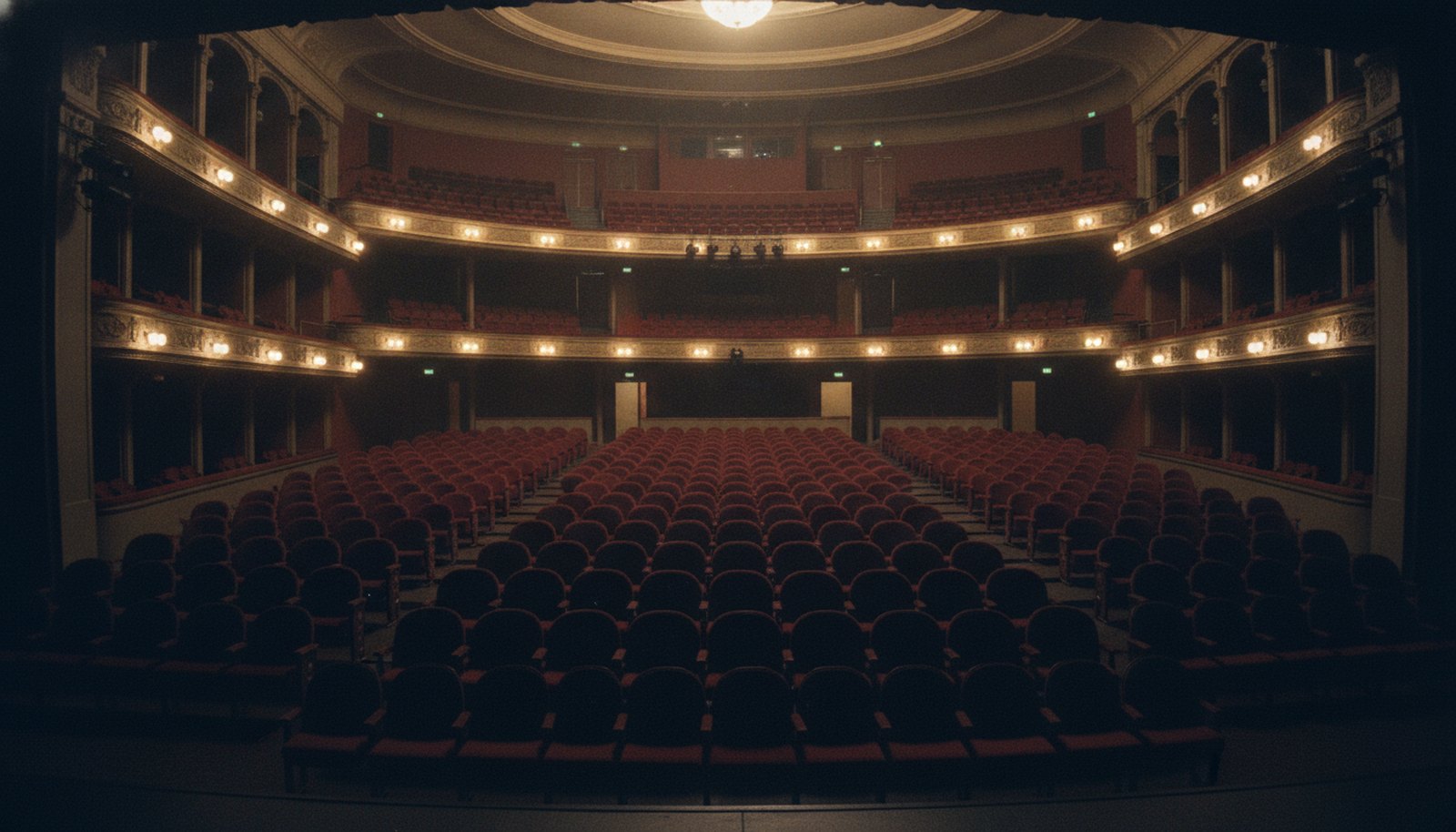 A theater interior lit in deep indigo and amber, empty seats facing a stage