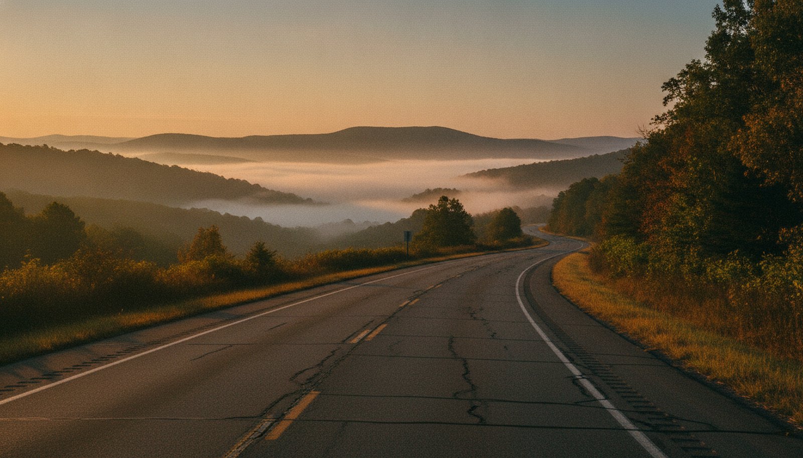 A two-lane highway at dawn winding through misty Blue Ridge foothills